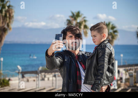 Father and son outdoors, father taking selfie using smartphone Stock Photo