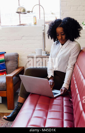 Woman in office sitting on sofa using laptop Stock Photo