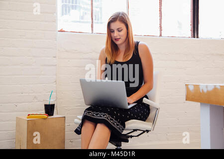 Woman in office chair using laptop Stock Photo