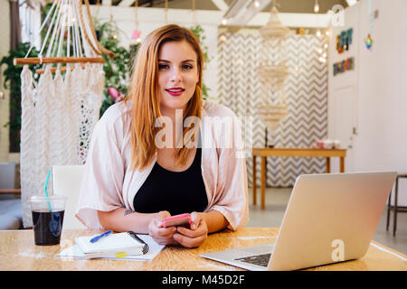 Woman sitting at desk in creative studio looking at camera smiling Stock Photo