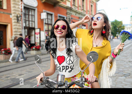 Portrait of two happy female friends wearing sunglasses riding scooter on cobbled street, Odessa, Ukraine Stock Photo