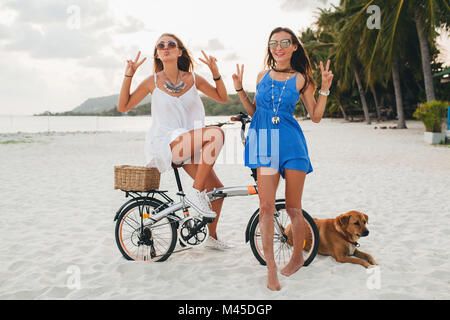 Portrait of two young women with bicycle making peace sign on sandy beach, Krabi, Thailand Stock Photo