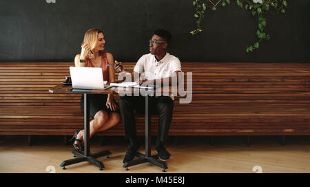 Business partners at a coffee shop working on a laptop computer. Friends sitting at a coffee table with laptop and notepads doing work. Stock Photo