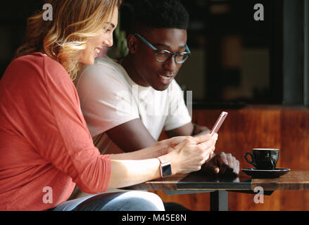 Couple sitting at a coffee shop using mobile phone. Man and woman sitting at a coffee table looking at a mobile phone. Stock Photo