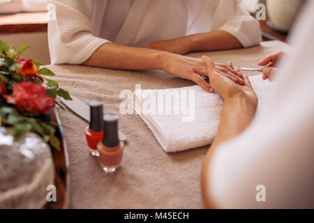 Manicurist shaping female clients nails at beauty salon. Woman hands in salon receiving a manicure by beautician. Stock Photo