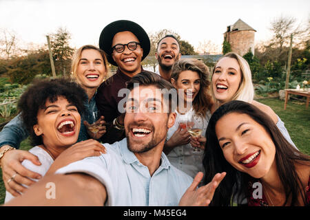 Friends chilling outside taking group selfie and smiling. Laughing young people standing together outdoors and taking selfie. Stock Photo