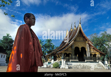 Laos. Luang Prabang. Royal Palace. Haw Pha Bang buddhist temple. Buddhist monk passing temple. UNESCO World Heritage Site. Stock Photo