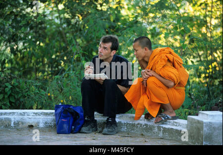 Laos. Luang Prabang. Wat Pha Phutthabaat buddhist temple. Buddhist monk sitting with man sketching. UNESCO World Heritage Site. Stock Photo