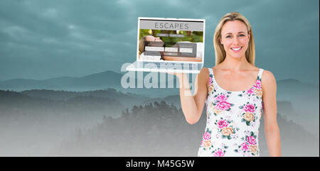 Composite image of smiling blonde holding laptop and posing Stock Photo