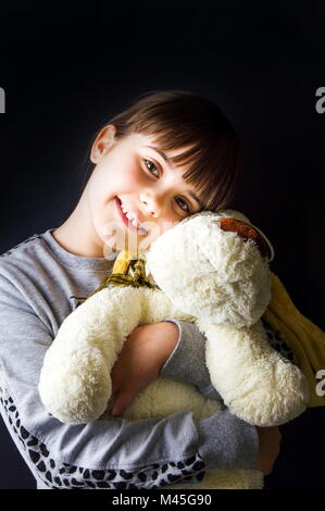 Cute little girl hugging her toy against dark background Stock Photo