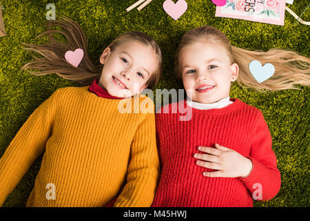 top view of happy little sisters lying on carpet surrounded with hearts Stock Photo