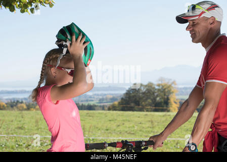 Father watching girl cyclist putting on bicycle helmet Stock Photo