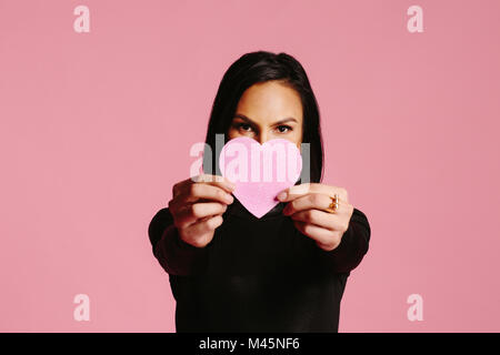 Woman in black showing pink heart covering half her face, be my valentine Stock Photo