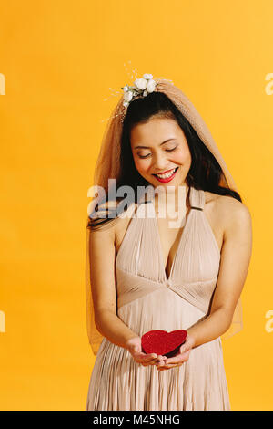 Asian bride in beige wedding dress holding a red heart isolated on orange Stock Photo