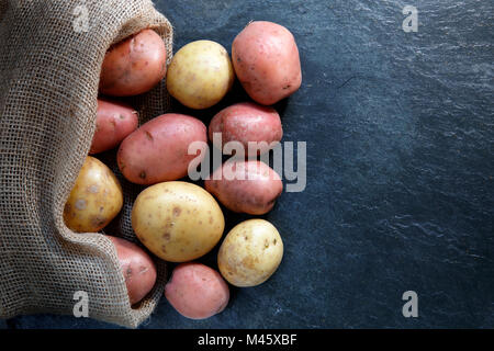 Red and Gold potatoes in hessian sack on slate table top with copy space Stock Photo