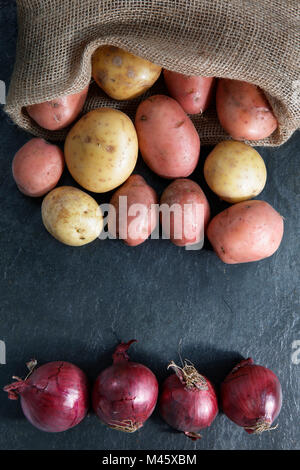 Red and Gold potatoes in hessian sack with red onions on slate table top with copy space - vertical portrait format Stock Photo