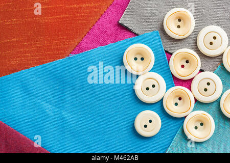 sewing, patchwork, tailoring and fashion concept - closeup on set of white buttons for needlework on a background of purple, red, blue and gray fabric Stock Photo