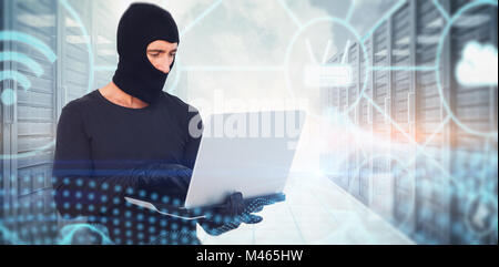 Composite image of burglar with balaclava hacking a laptop Stock Photo