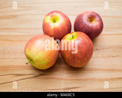 Four colourful Pink Lady eating apples variety Cripps Pink on a wooden board Stock Photo