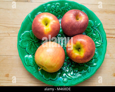 Four colourful Pink Lady eating apples variety Cripps Pink on a green plate Stock Photo