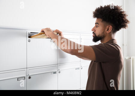 Side View Of A Young Man Putting Letters In Mailbox Stock Photo