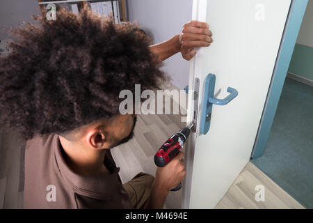 Close-up Of A Young Male Carpenter Installing Door Lock With Wireless Screwdriver Stock Photo
