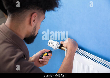 Close-up Of A Young Male Plumber Installing Radiator With Screwdriver Stock Photo