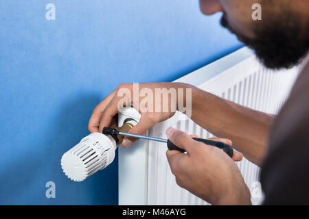 Close-up Of A Young Male Plumber Installing Radiator With Screwdriver Stock Photo