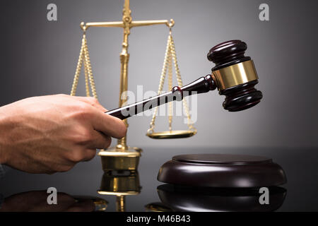 Judge Striking Gavel On Sounding Block In Front Of Golden Weighing Scale Stock Photo