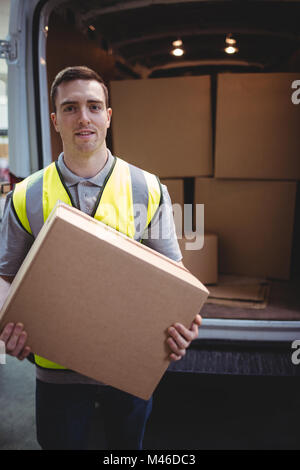 Delivery driver smiling at camera by his van holding parcel Stock Photo