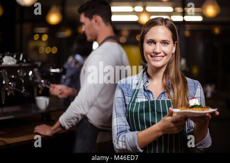 Pretty barista holding dessert and smiling at the camera Stock Photo
