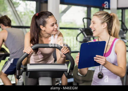 Trainer woman talking with a woman doing exercise bike Stock Photo