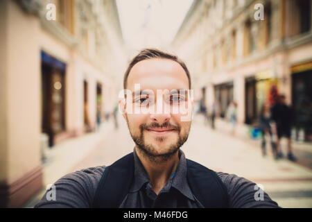 Portrait of a happy man with beard taking selfie. Hipster tourist smiles into the camera. Blurred background. Stock Photo