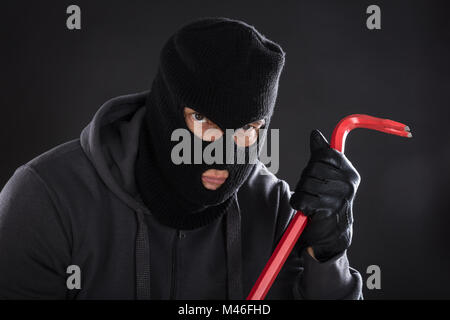 Portrait Of A Burglar Wearing Balaclava Holding Crowbar On Black Background Stock Photo