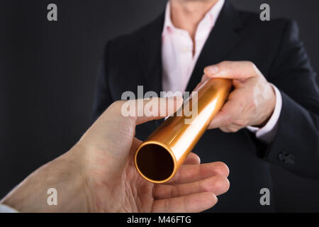 Close-up Of A Businessman Passing Golden Relay Baton To Colleague Stock Photo