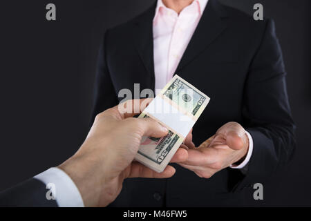 Close-up Of A Businessman Receiving A Bank Note On Black Background Stock Photo