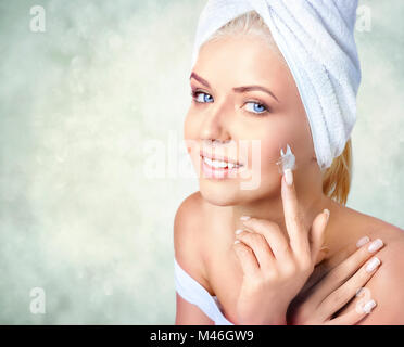 Close-up portrait of beautiful smiling woman with towel on hair, applying moisturizing cream Stock Photo