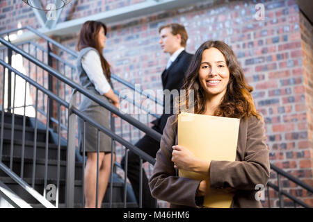 Businesswoman standing near staircase with documents Stock Photo