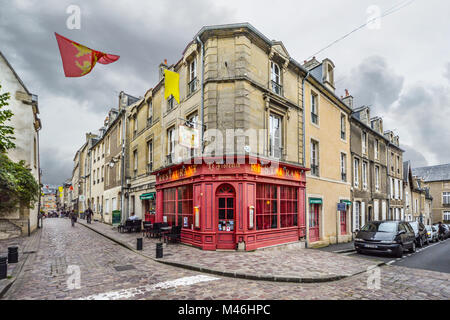 The colorful red facade front of a restaurant on a corner intersection in the Normandy town of Bayeux France with tables on the sidewalk. Stock Photo