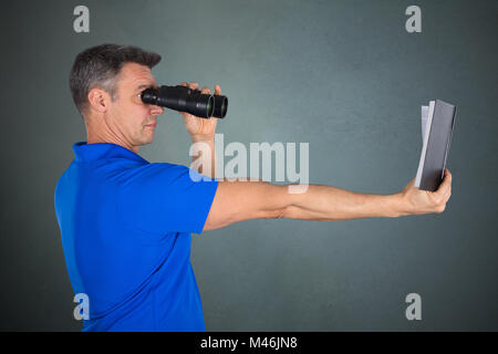 Matured Man With Hyperopia Eye Disorder Reading A Book Using Binocular On Gray Background Stock Photo