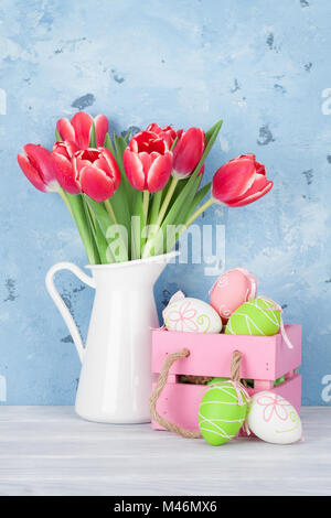 Red tulip flowers bouquet in pitcher and easter eggs in front of wooden wall.  Easter greeting card Stock Photo