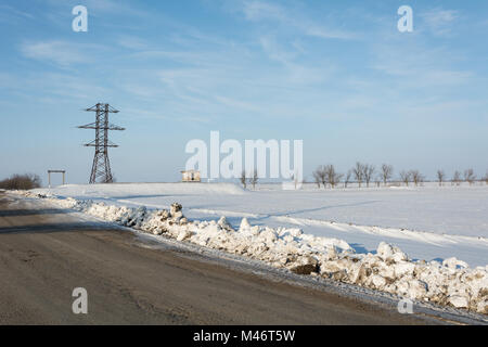 Electrical power line pillar on snow in front of blue sky and clouds Stock Photo