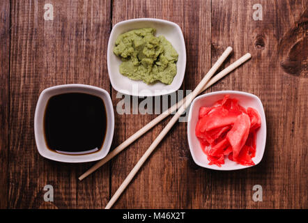 Sticks, Wasabi, soy sauce and pickled ginger for sushi on brown wooden table background. Top view. Stock Photo
