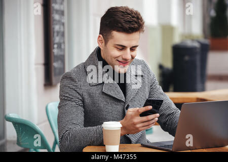 Portrait of successful guy resting in street cafe, working with notebook and typing text message on his mobile phone Stock Photo