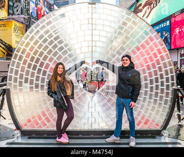 New York, USA,  14 Feb 2018.  A couple pose next to the 'Window to the Heart', a twelve-foot round resin lens with a heart shaped center placed in New York's Times Square.. The art installation became a popular destination on Valentine's Day.   Photo by Enrique Shore/Alamy Live News Stock Photo