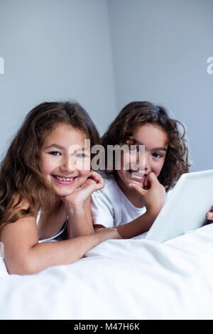 Portrait of brother and sister using digital tablet lying on sofa in ...