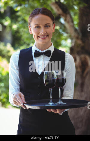 Smiling waitress holding a tray with glasses of red wine Stock Photo