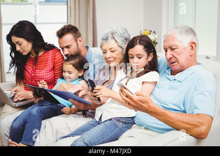 Family using technologies while sitting on sofa Stock Photo