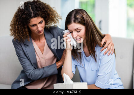 Female psychologist consoling depressed woman on sofa at home Stock Photo