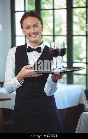 Smiling waitress holding a tray with glasses of red wine Stock Photo